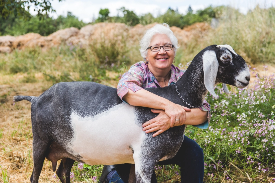 a woman hugging a goat in a field of flowers