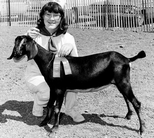 A woman kneeling down with a goat and a winner ribbon